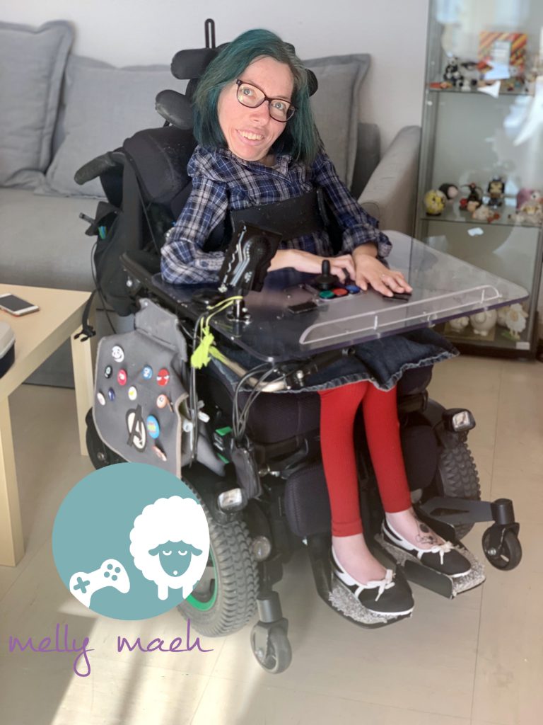 Melly lächelt in die Kamera. Sie trägt eine blaue, karrierte Bluse, einen Jeansrock und eine rote Leggins. Sie sitzt in einem elektrischen Rollstuhl.